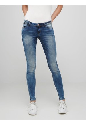 Jeans ajustados de mezclilla azul con un lavado deslavado, diseño de cinco bolsillos, cierre de botón y bucles para cinturón, combinados con zapatillas blancas.