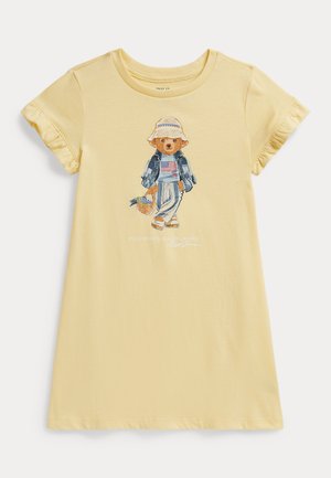 Sárga pamut póló fodros ujjakkal, nyomott mintával, amely egy farmernadrágot és kalapot viselő medvét ábrázol, aki egy kosarat tart. Laza szabás.