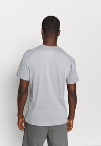 Camiseta de manga corta gris claro con un patrón texturizado en la parte posterior, cuello redondo y aberturas en los lados para facilitar el movimiento.