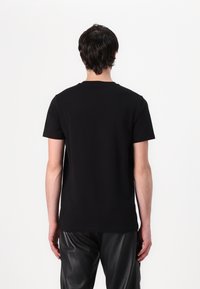 T-shirt noir à encolure ras du cou, à manches courtes et à la texture de tissu lisse, accompagné d'un pantalon en cuir noir ample.