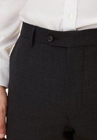 Dunkelgraue maßgeschneiderte Hose aus strukturiertem Stoff, mit einem Knopfverschluss und Seitentaschen, getragen mit einem weißen Hemd mit Knopfleiste.