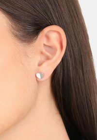 Pendientes de plata en forma de corazón que presentan un acabado medio mate y medio pulido, llevados en el lóbulo de la oreja, con una textura suave.