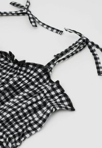 Schwarz-weißer Gingham-Stoff-Oberteil mit verstellbaren Bindeträgern, Rüschenkanten und geraffter Textur, die das kariertes Muster betont.