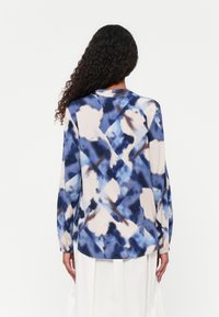 Langärmlige Bluse mit einem blauen und beigen abstrakten Muster, aus leichtem Stoff gefertigt, mit lockerer Passform und rundem Ausschnitt.