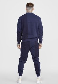 Chándal de algodón azul navy con cuello redondo, mangas largas y puños elásticos. Incluye detalles de costura y panel texturizado en la parte posterior.