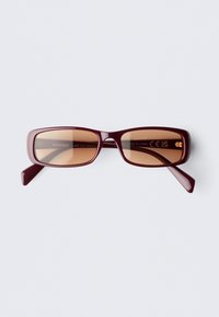 Óculos de sol retangulares cor borgonha com lentes castanhas. Armação em plástico com bordas limpas e uma marcação subtil nos braços interiores.