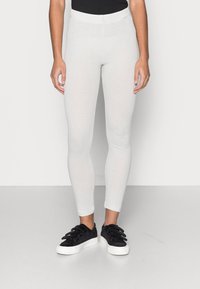 Leggings brancos texturizados com um design ajustado e faixa elástica na cintura, combinados com ténis pretos texturizados com uma sola branca.