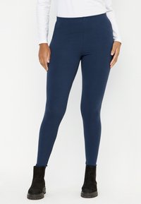 Marineblauwe leggings gemaakt van een zachte, rekbare stof. Hooggesneden ontwerp met een gladde afwerking, gecombineerd met zwarte enkelboots.