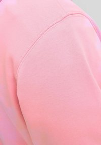 Tessuto di felpa rosa con una texture liscia, caratterizzato da una cucitura lungo la spalla e un collo leggermente curvo.