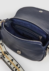 Mörkblå lädercrossbodyväska med dragkedjestängning. Inuti har väskan ett tygfoder, en dragkedjeficka och en justerbar mönstrad rem med logotyp.