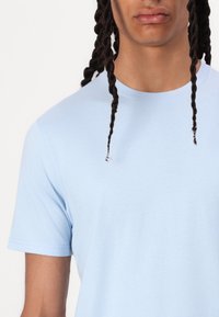 Ανοιχτό μπλε κοντομάνικο T-shirt με στρογγυλή λαιμόκοψη και απαλό, λείο υφή. Διαθέτει τυπική ραφή στα μανίκια και το στρίφωμα.