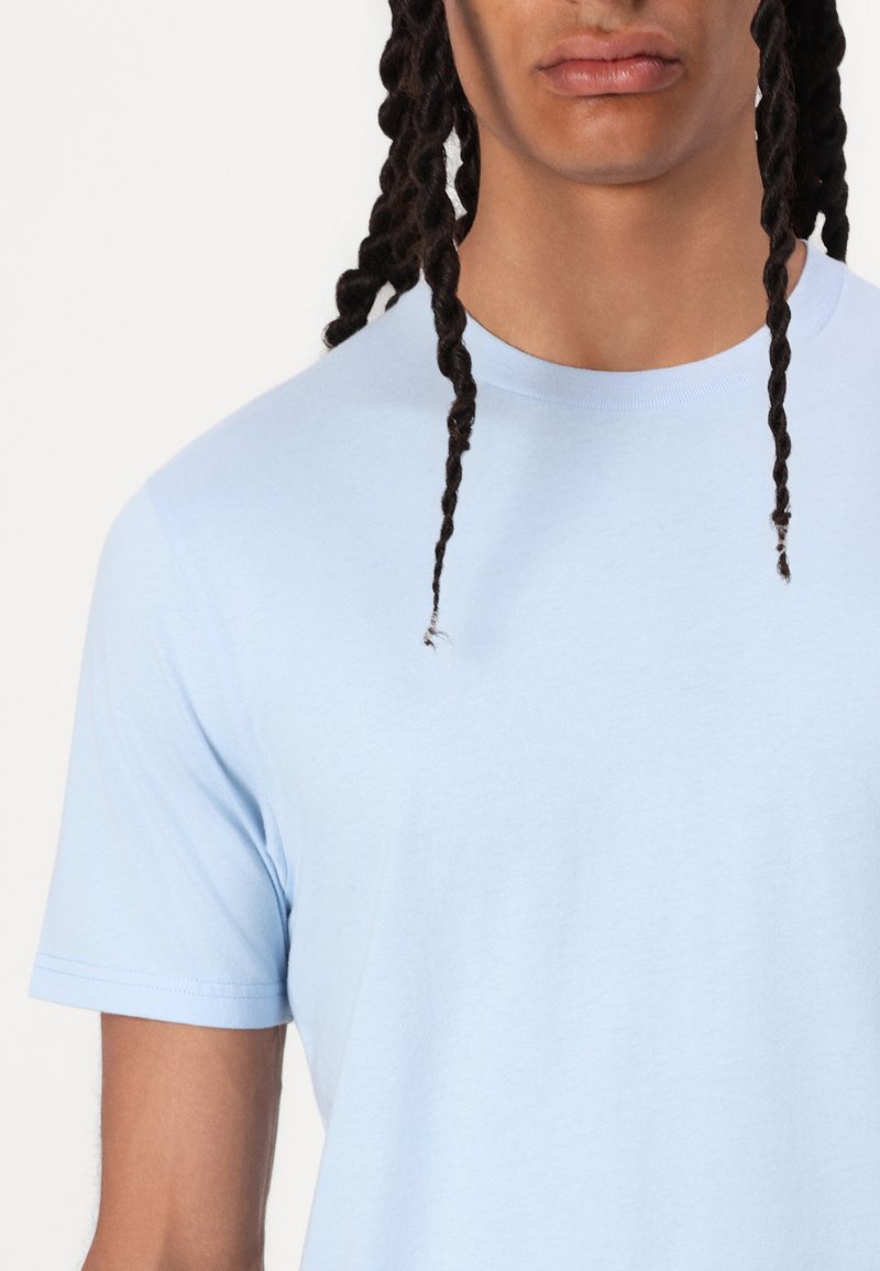 Camiseta de manga corta azul claro con cuello redondo y una textura suave y lisa. Presenta costuras estándar en las mangas y el dobladillo.