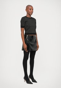 Cropped top nero con motivo testurizzato, mini gonna in pelle nera lucida, collant neri opachi e décolleté neri a punta con dettagli dorati.