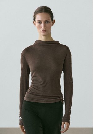 Hnědý top s dlouhým rukávem a šálovým výstřihem, texturovaná látka, přiléhavý střih a na straně shromážděný detail, ve spojení s černými legínami.