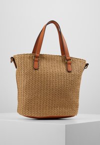Geweven stro tote tas in lichtbruin met bruine lederen accenten, dubbele handvatten en een gestructureerde vorm met een getextureerd oppervlak.