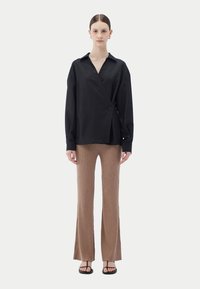 Svart omlottsblus med krage och knäppning framtill; kombinerad med bruna ribbade utsvängda byxor och svarta plana sandaler.