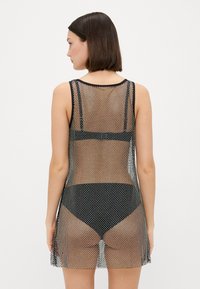 Abito in rete nera con design senza maniche, caratterizzato da un motivo testurizzato. La schiena è semitrasparente, sovrapposta a uno slip nero.