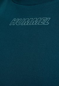 Teal sporttop gemaakt van textiel met een gestructureerde stof, voorzien van een opvallend "HUMMEL" logo in lichtblauw op de bovenste borstkas.