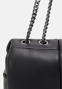 Borsa nera in pelle sintetica con un design trapuntato, dotata di doppi manici a catena e grommet circolari per l'attacco.