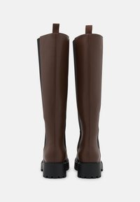 Botas marrones hasta la rodilla con un diseño elegante, hechas de cuero liso y laterales elásticos. Suelas gruesas de goma negra con un ligero patrón de tracción.