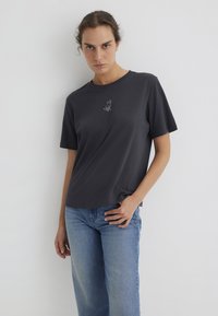 Dark gray short-sleeve t-shirt made of soft fabric featuring a small white dog graphic on the chest. Worn with light blue jeans.