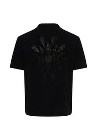 Chemise noire à manches courtes avec col, présentant un motif perforé en forme de rayons de soleil centré dans le dos.