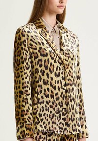 Blazer con stampa leopardata in tessuto setoso, caratterizzato da un colletto a revers, design monopetto e una vestibilità elegante. Rifinito con dettagli a bottoni.