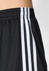 Black athletic shorts feature a stretchy waistband with three white stripes along the side, made from smooth, lightweight fabric.
