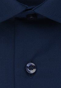 Tessuto di camicia cotone blu navy con una texture liscia, dotato di un bottone nero a quattro fori e un design colletto classico.