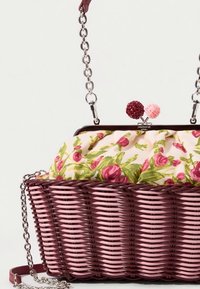 Sac panier tissé en bordeaux et rose. Dispose d'une doublure en tissu à motif floral et d'une bandoulière chaîne argentée avec deux fermoirs décoratifs.