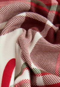 Tekstilą puošia minkštas, audinys su raudonomis, žaliomis ir grietinėlės spalvos juostelėmis bei šachmatų raštu. Audinys atrodo jaukus ir tekstūruotas.