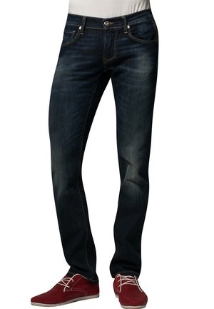 Dunkelblaue Slim-Fit-Jeans, getragen mit roten Schnürschuhen, zeigen Vordertaschen, Gürtelschlaufen und dezentes Verblassen an den Oberschenkeln.