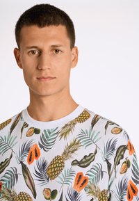 Vit t-shirt med ett färgglatt tryck av tropiska frukter och blad, med ananaser och papayer. Rund halsringning och korta ärmar.