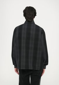 Camisa xadrez preta com corte descontraído, apresentando um colarinho alto e mangas longas, feita de tecido suave com uma textura subtil.