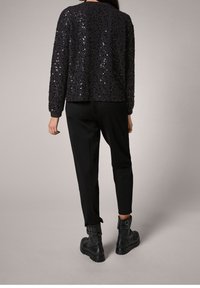 Top negro con lentejuelas y mangas largas, combinado con pantalones negros y botas negras con hebilla en el tobillo. Textura suave con acabado brillante.