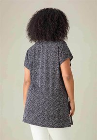 T-shirt tunica a maniche corte nera con un motivo geometrico bianco, caratterizzata da una vestibilità rilassata, fenditure laterali e una texture del tessuto liscia.