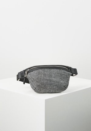 Czarna i biała torba na pas z tkaniny w wzór pepitki, z czarną skórzaną lamówką zamka błyskawicznego oraz regulowanym paskiem, prezentowana na białym piedestale.