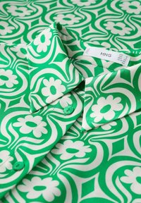 Chemise à motifs verts et blancs avec un motif floral, tissu lisse, col boutonné et boutons verts. Étiquette visible avec la taille et la marque.