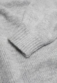 Manche de pull en tricot gris clair avec poignet côtelé, montrant un fil texturé doux et duveteux et des détails de points en gros plan.