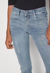 Vaaleansiniset farkut, joissa on kulutustyylisiä yksityiskohtia, viisi taskua ja nappikiinnitys. Farkut ovat slim fit -malliset ja niissä on hienovarainen haalistus.