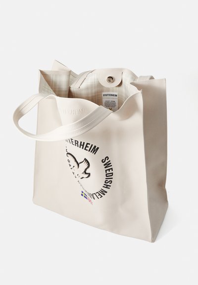 Borsa tote impermeabile beige con una stampa grafica di una colomba e testo. Presenta una texture liscia e due manici robusti. L'interno è a quadri.