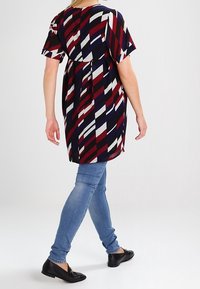 Kuviollinen mekko lyhyillä hihoilla tummansinisessä, punaisessa ja valkoisessa geometrisessä kuosissa; päällä vaaleansiniset skinny-farkut ja mustat ballerinat.