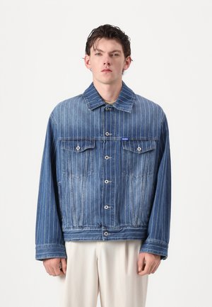Jachetă din denim albastră cu dungi verticale albe, închidere cu nasturi, două buzunare pe piept și o croială relaxată. Prezintă eticheta de brand pe față.