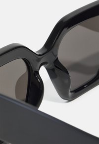 Black sunglasses featuring a thick, glossy frame with a unique cutout design. Dark lenses and smooth texture emphasize modern aesthetics.