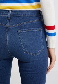 Blå denimjeans med en figurnära design, med en bakficka, stickade detaljer och en mjuk textur.