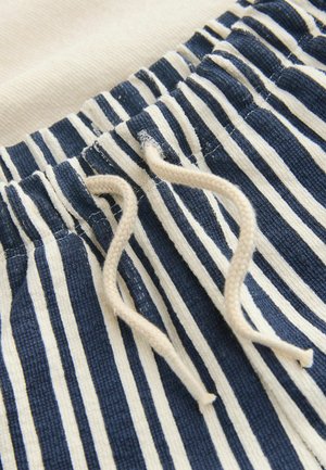 Nahaufnahme eines blau-weiß vertikal gestreiften Stoffs mit beigefarbenem Kordelzug, der durch gestickte Ösen gebunden ist.