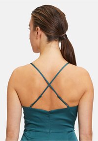 Robe teal avec un corsage ajusté et des bretelles croisées dans le dos, dotée d'une fermeture éclair et de texture lisse, semblable à du satin.