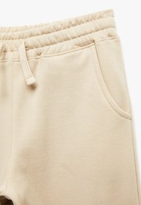 Beige svettbyxor med en mjuk textur, elastisk midja, dragsko och sidofickor. Har släta sömmar och minimalistisk design.