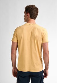 Žluté bavlněné tričko s krátkým rukávem a kulatým výstřihem, pohled zezadu. Hladká textura s volným střihem a jednoduchým designem.