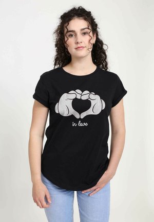 Schwarzes Baumwoll-T-Shirt mit einem silbernen Grafikdesign, das Hände zeigt, die ein Herz bilden, begleitet von dem Text "in love" unter dem Design.